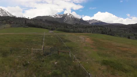 snow covered rocky mountains and open ranch hillside fly over tall grass during the spring