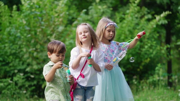 Children with bubble blower in their hands over the nature background. Two little girls and a cute small boy are blowing bubbles in the park.