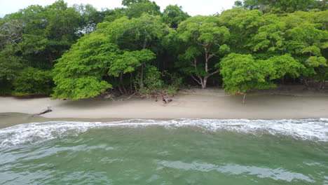 Luftaufnahme-Einer-Frau,-Die-An-Einem-Tropischen-Strand-Mit-Türkisfarbenen-Wellen-Im-Parque-Nacional-Manuel-Antonio,-Costa-Rica,-Steht