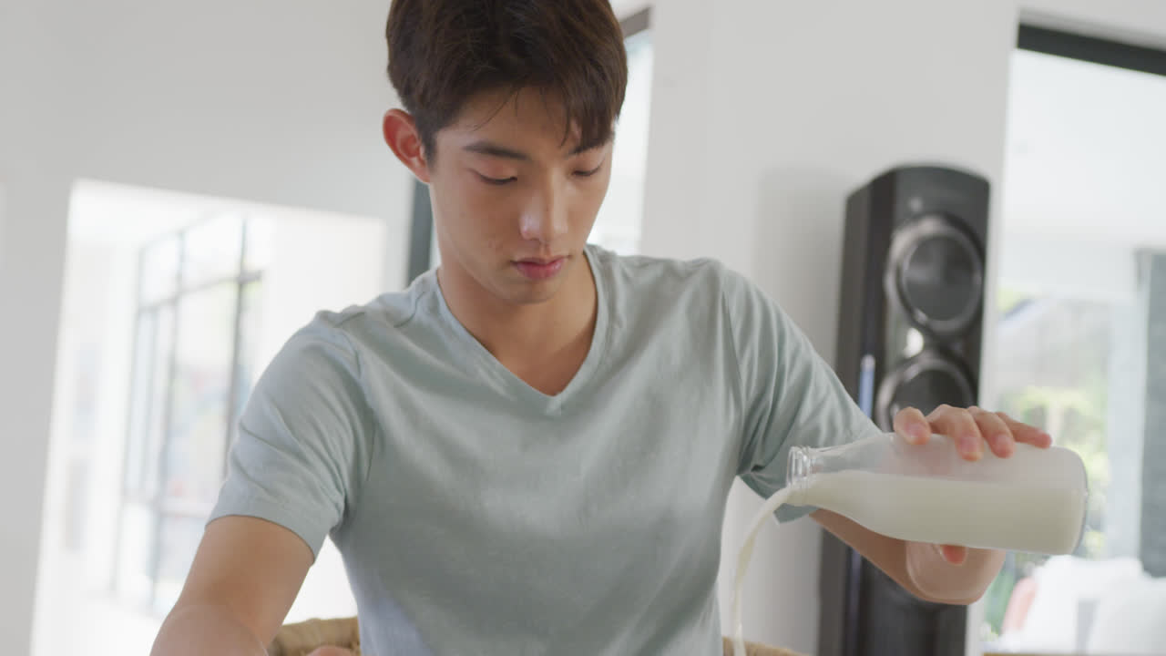 아시아 소년 이 집 에서 시리얼 그 에 우유 를 부어 놓고 있다