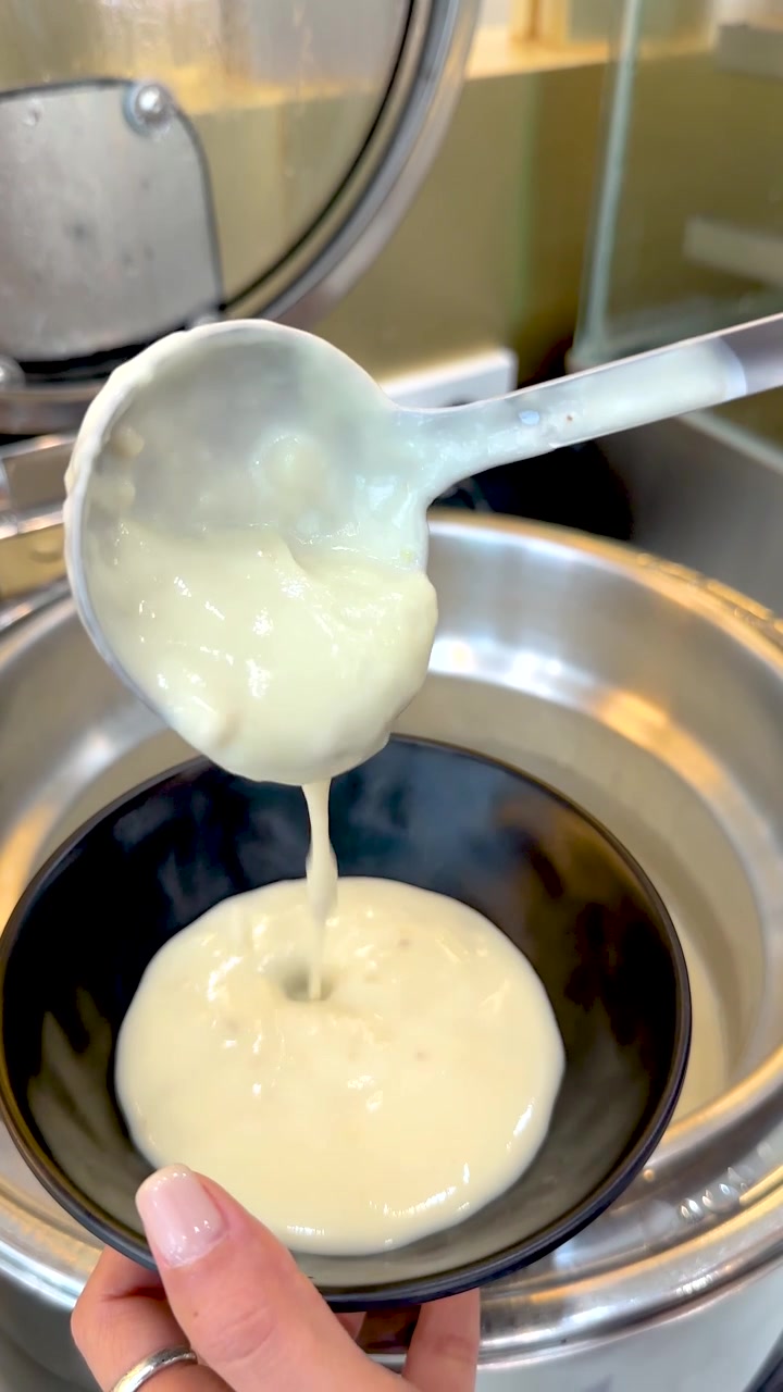 Close-up shot of a hand pouring hot creamy soup from a stainless steel buffet warmer