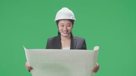 smiling asian female engineer with safety helmet looking at blueprint in the green screen studio