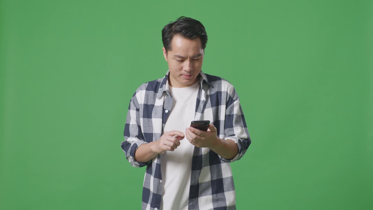 스튜디오 에서 녹색 스크린 을 걸으면서 휴대 전화 를 사용하는 아시아인