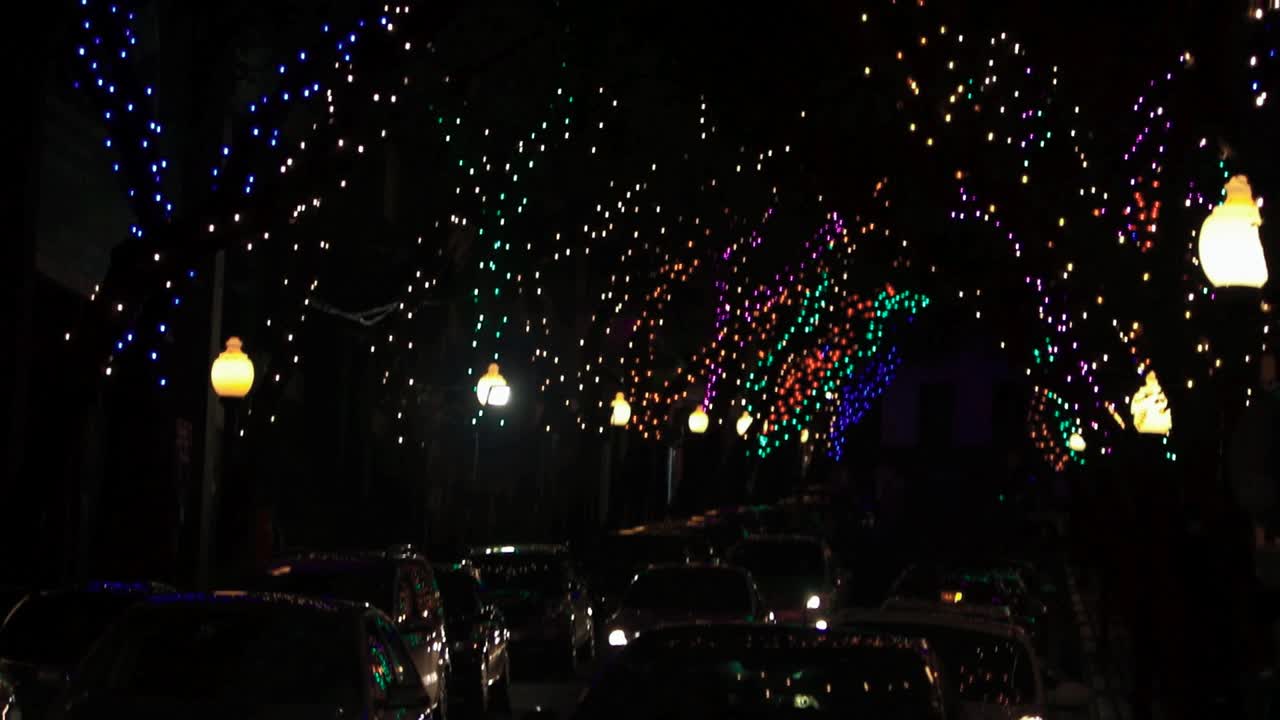 Various cars driving at night through downtown city streets with decorated trees for christmas festive season bright colorful lights Madeira Island celebrating xmas graded reveal tilt HD background