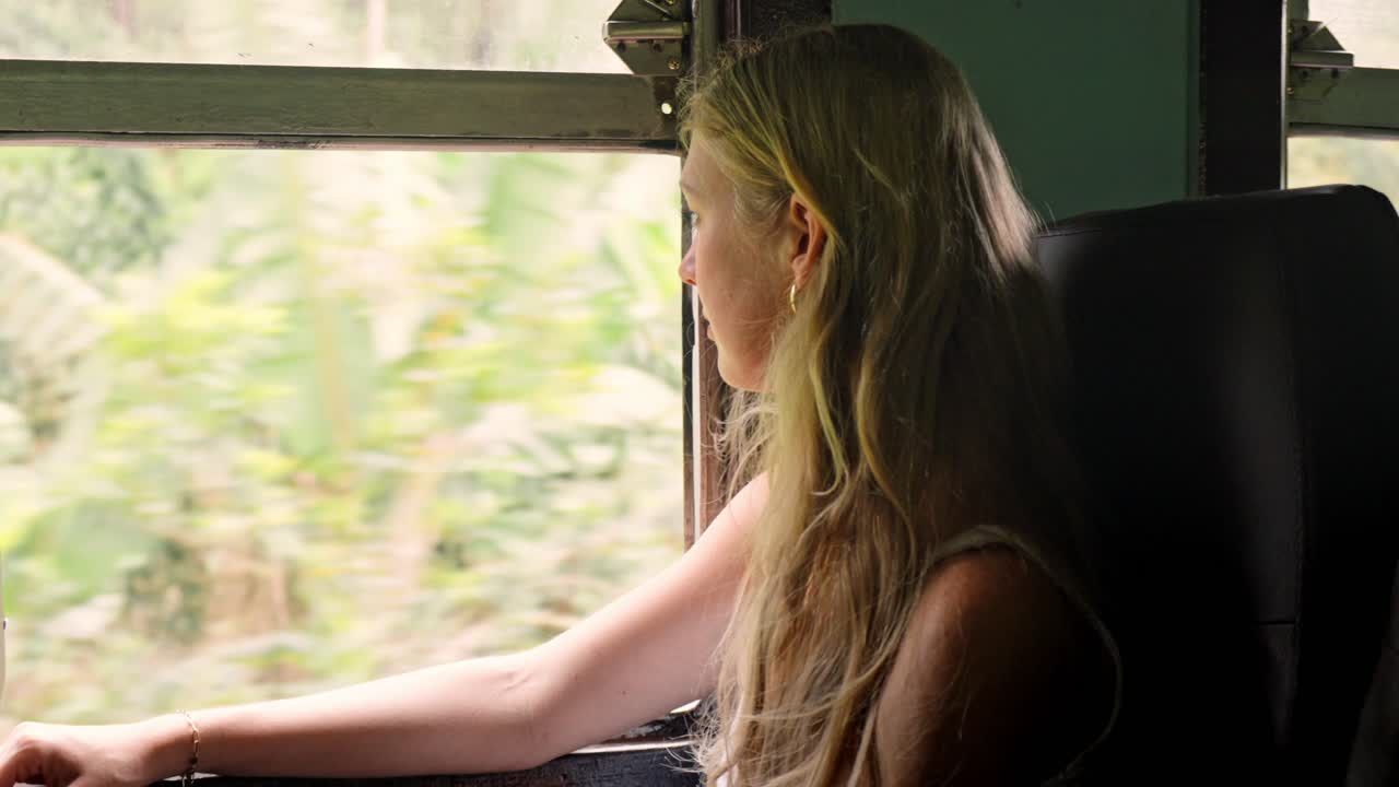 A woman sits peacefully inside a Sri Lankan train, gazing out the window at the lush green jungle that flanks the iconic Ella to Kandy railway.