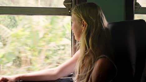 a woman sits peacefully inside a sri lankan train, gazing out the window at the lush green jungle that flanks the iconic ella to kandy railway.