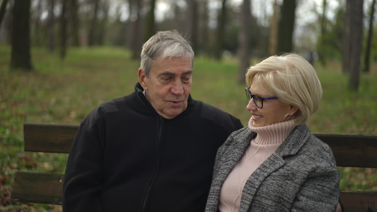 Пожилая пара сидит на скамейке в парке.