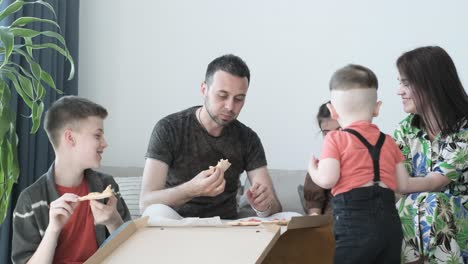 happy family eating pizza sitting on sofa at home happy family eating pizza sitting on sofa at home husband and wife with children eating delicious italian pizza out of the box pizza home delivery