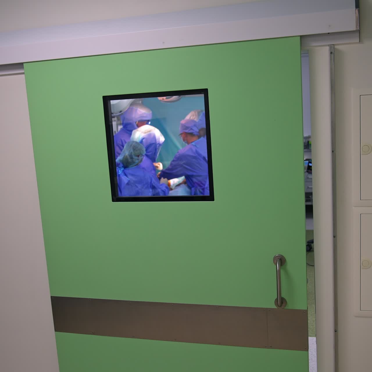 Standing in the hall near the doors to the modern surgical theatre. Doctor's team performing surgery in the room