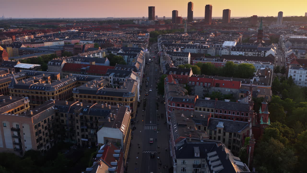 Aerial drone view down a long Copenhagen avenue lined with historic apartments and rooftops, with modern towers in the distance in Denmark