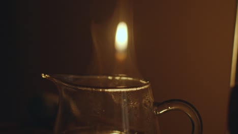 close-up shot of steam pour out from glass jar in slow motion. transparent teapot with hot chinese tea candle light on background. teaware equipment for traditional tea ceremony asian culture concept