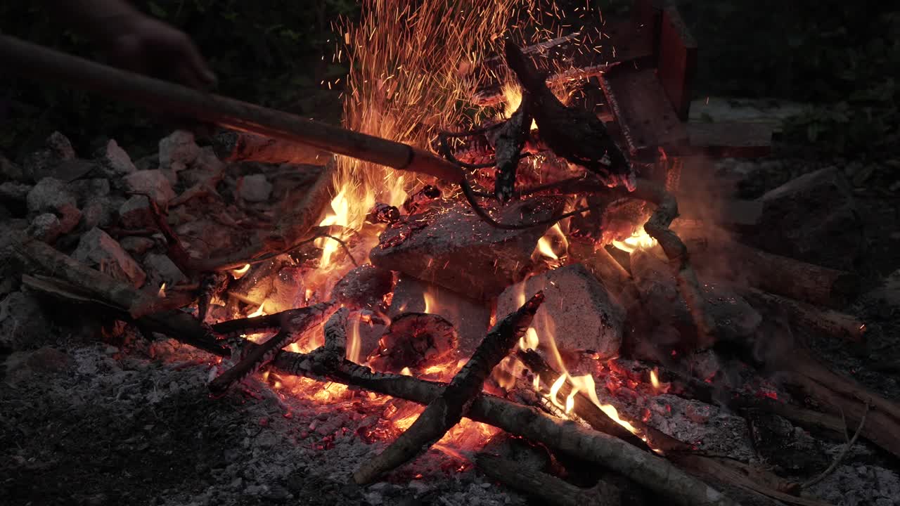 Campfire for Temazcal in jungle, wood moving with fork, sparks fly up, gray stones around, dawn and evening time.