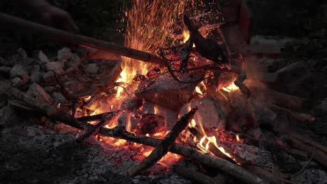 campfire for temazcal in jungle, wood moving with fork, sparks fly up, gray stones around, dawn and evening time.