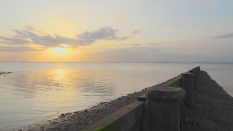 Langsamer-Aufstieg-über-Den-Wellenbrecher-Mit-Schiffen-Am-Horizont-Während-Des-Sonnenuntergangs-In-Zeitlupe-In-Fleetwood,-Lancashire,-Großbritannien