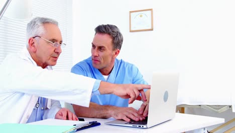 médico masculino y colega discutiendo en la computadora portátil