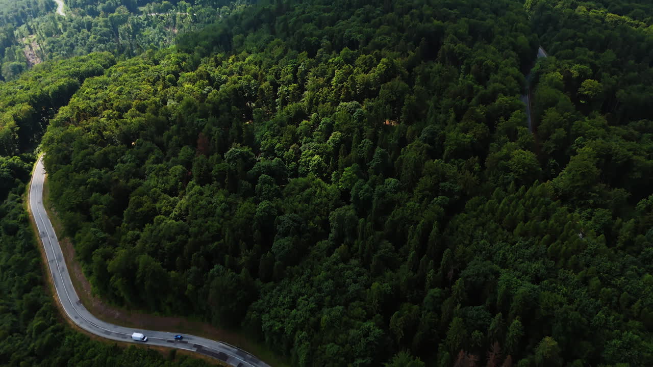 Amazing dark thick forests cover the rocky landscape. Cars run by the highway in the woods. Aerial view.