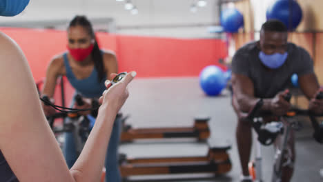 Caucasian-female-fitness-trainer-using-stopwatch-at-gym