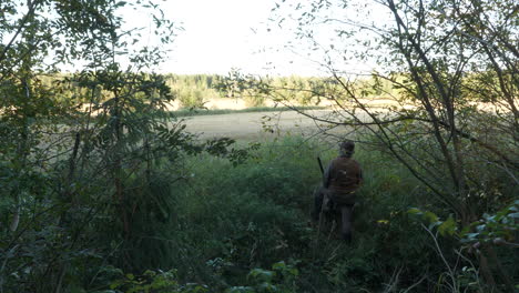 Hunter-hiding-in-bushes-and-grass,-scouting-field-for-potential-target,-10-bit-flat-color-profile