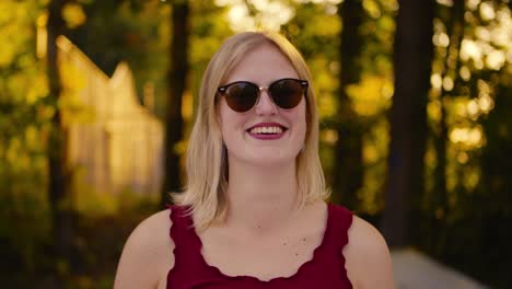 Girl-puts-on-her-sunglasses-in-a-park-and-then-smiles-into-the-camera-and-moves-her-hand-through-her-hair