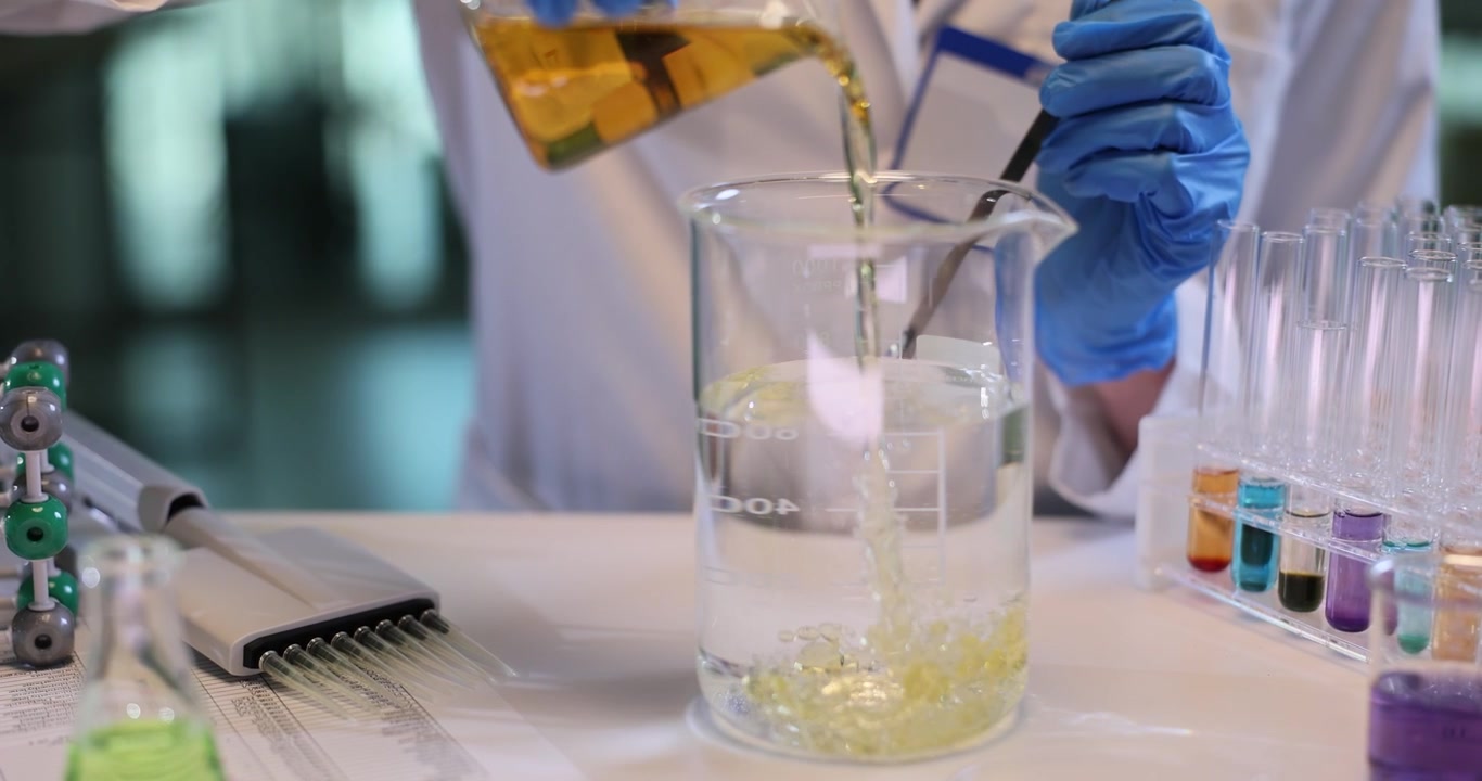 Female assistant pours oil into water and stirs in chemical lab