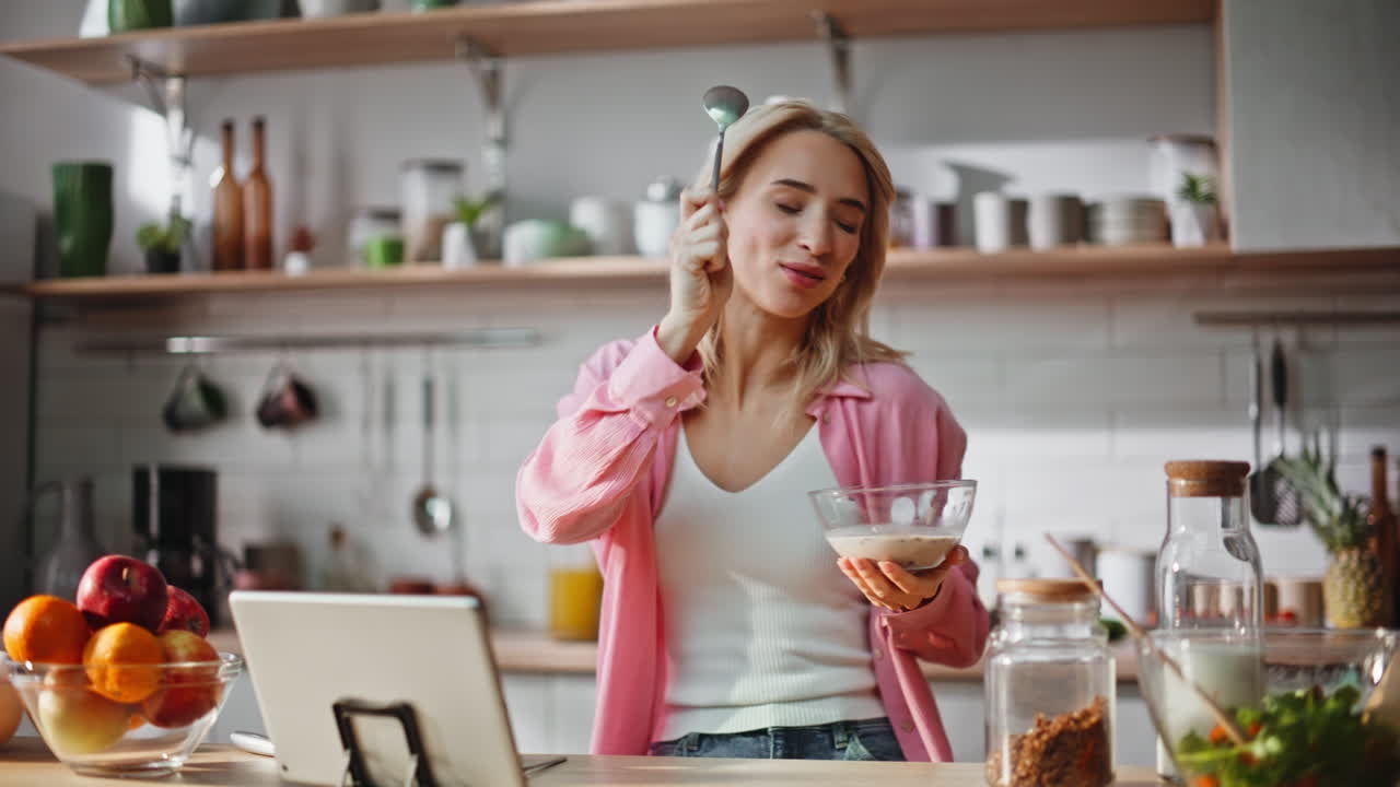 Morning blonde eating breakfast enjoying music on tablet at kitchen closeup
