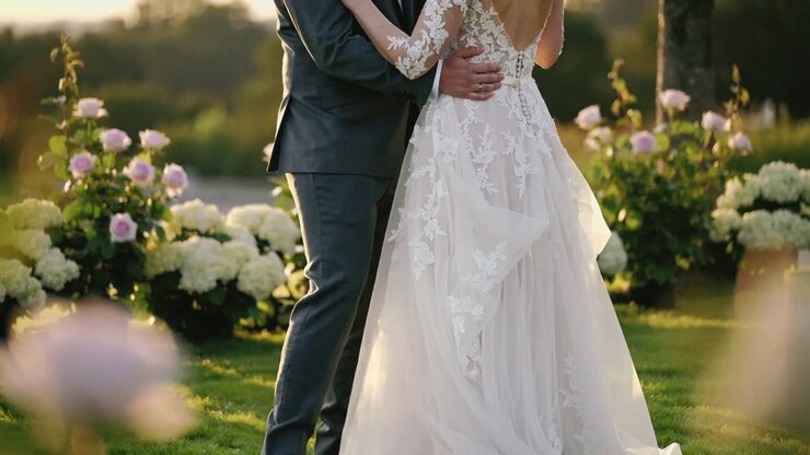 Zooming camera revealing bride and groom embracing on grassy lawn, showing lace gown back details