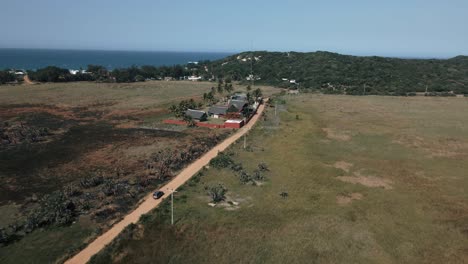 Toma-Aérea-De-Seguimiento-De-Un-Automóvil-Conduciendo-Por-El-Campo-De-Mozambique-Pasando-Por-Casas.