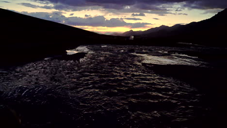 Tiro-Oscuro-Inclinado-Desde-Un-Río-Hasta-Una-Escena-De-Puesta-De-Sol-Sobre-Una-Cadena-Montañosa-En-El-Himalaya