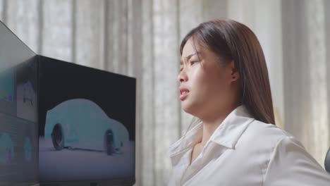 아시아 여성 자동차 디자이너가 스튜디오의 데스크 컴퓨터에서 ev 자동차의 3d 모델을 작업하는 동안 허리 통증을 겪는 가까운 측면 뷰