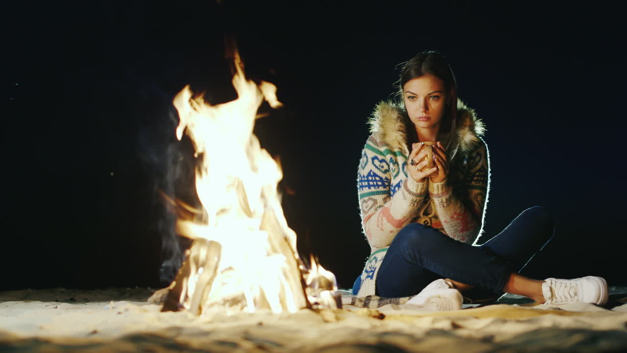 불 옆에 혼자 앉아 불을 바라보며 차를 마시는 젊은 여성