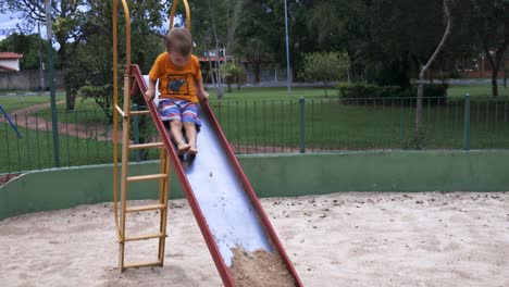 kid climbing up and then sliding down the slide with sand on the end during a bright day with trees in the background