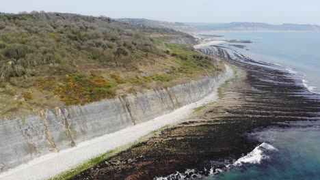 coastal cliffs overlooking a serene beach and pristine waters on a sunny day. aerial pan left shot