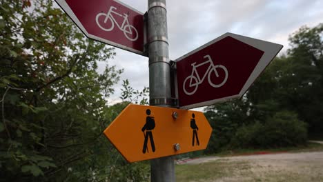 Close-up-shot-of-hiker-and-bicycle-sign-showing-path-and-track-in-swiss-mountain-landscape-during-cloudy-day---pullback-shot