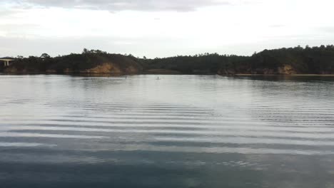 Low-angle-aerial-flying-over-moored-boats-toward-standup-paddleboarders-in-Milfontes