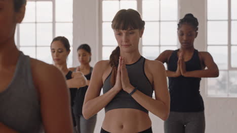 hermosa mujer caucásica de yoga practicando meditación en pose guerrera con un grupo de mujeres multirraciales disfrutando de un estilo de vida saludable haciendo ejercicio en un gimnasio al amanecer.