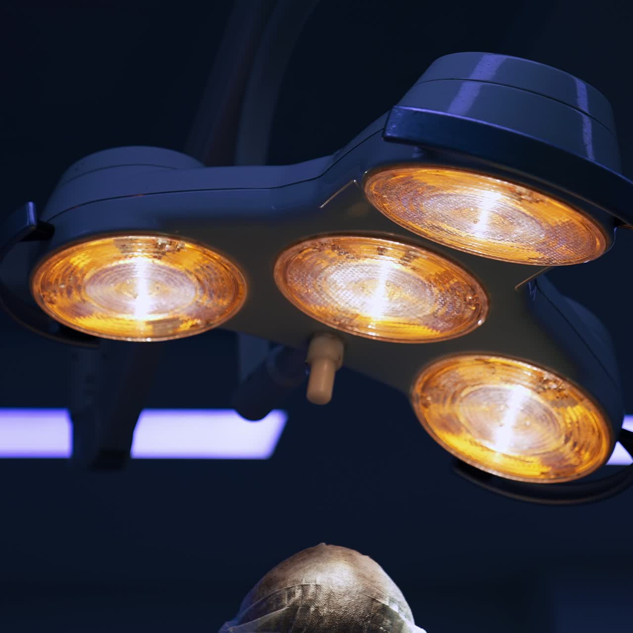 Lamp is on at the ceiling of surgical room. Doctors work under the dim illumination at operation