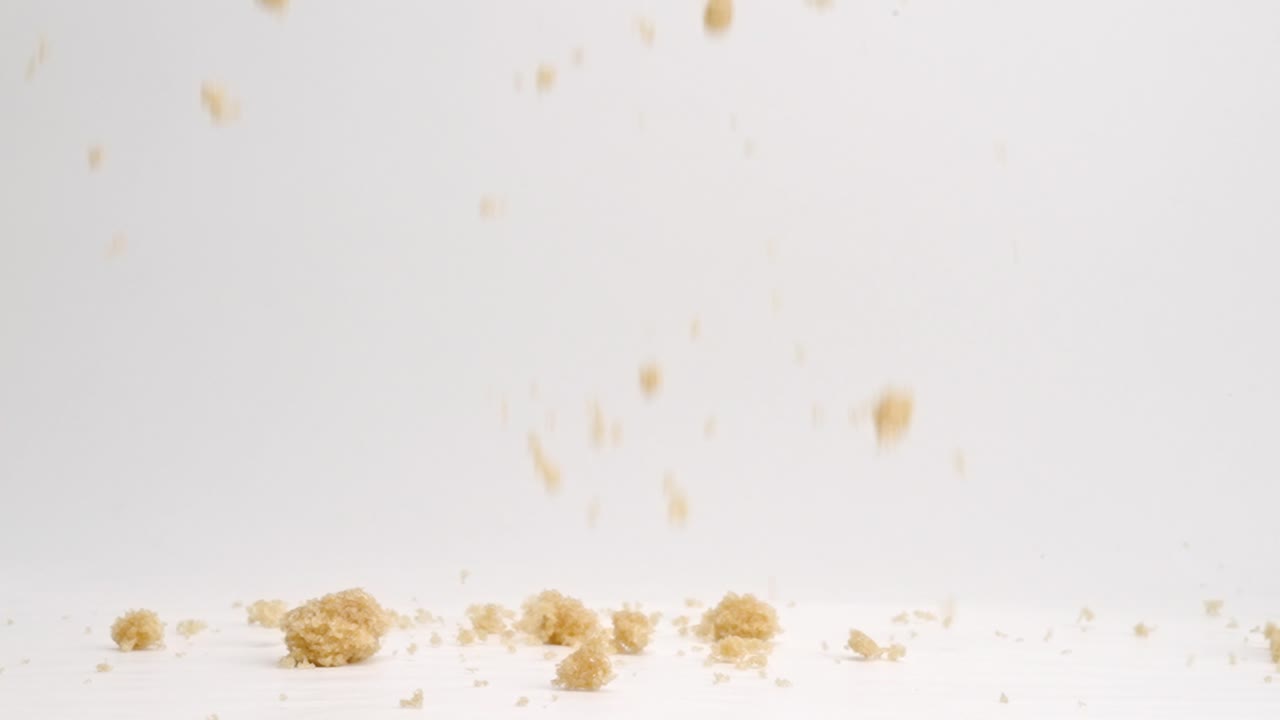 4k 느린 동작으로 흰색 스튜디오 배경에 떨어지는 갈색 설탕 조각