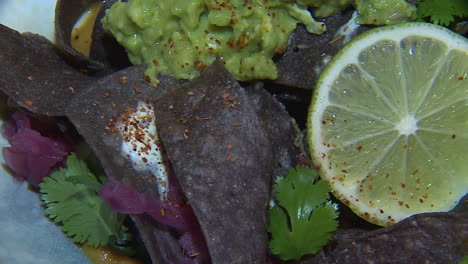 close-up of blue corn tortilla chips with guacamole, lime, and cilantro