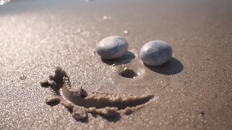 Sjovt ansigt på sandstrand lavet af sten og sand