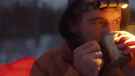 man drinking hot tea at campsite in evening