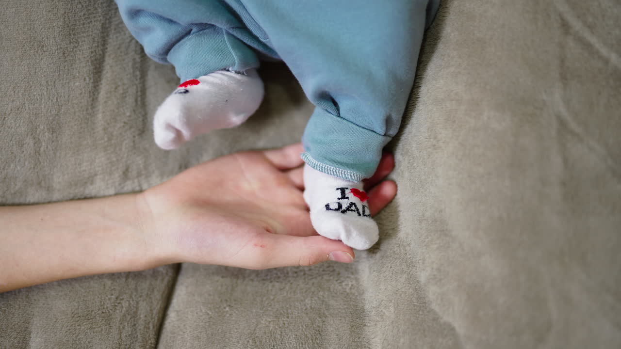 Mother is holding baby feet in her hand. Child tosses little feet in funny socks. Grey background.