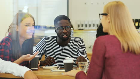 camera focuses on a multiethnic group of friends through the window talking sitting at a table in a cafe