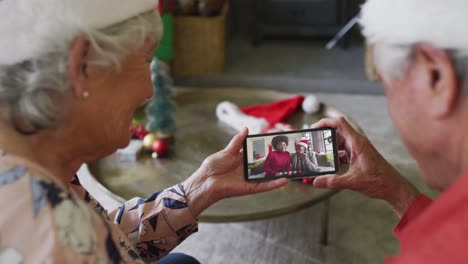 pareja caucásica mayor usando un teléfono inteligente para una videollamada de navidad con una familia sonriente en la pantalla