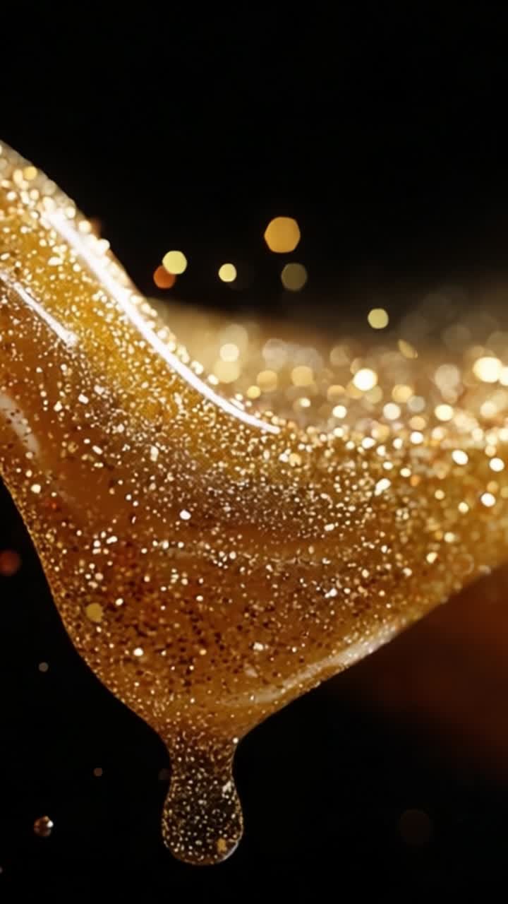 Oro liquido affascinante: un primo piano di fluido dorato scintillante che scorre con grazia su uno sfondo scuro, evidenziandone la texture lucente e le particelle scintillanti.