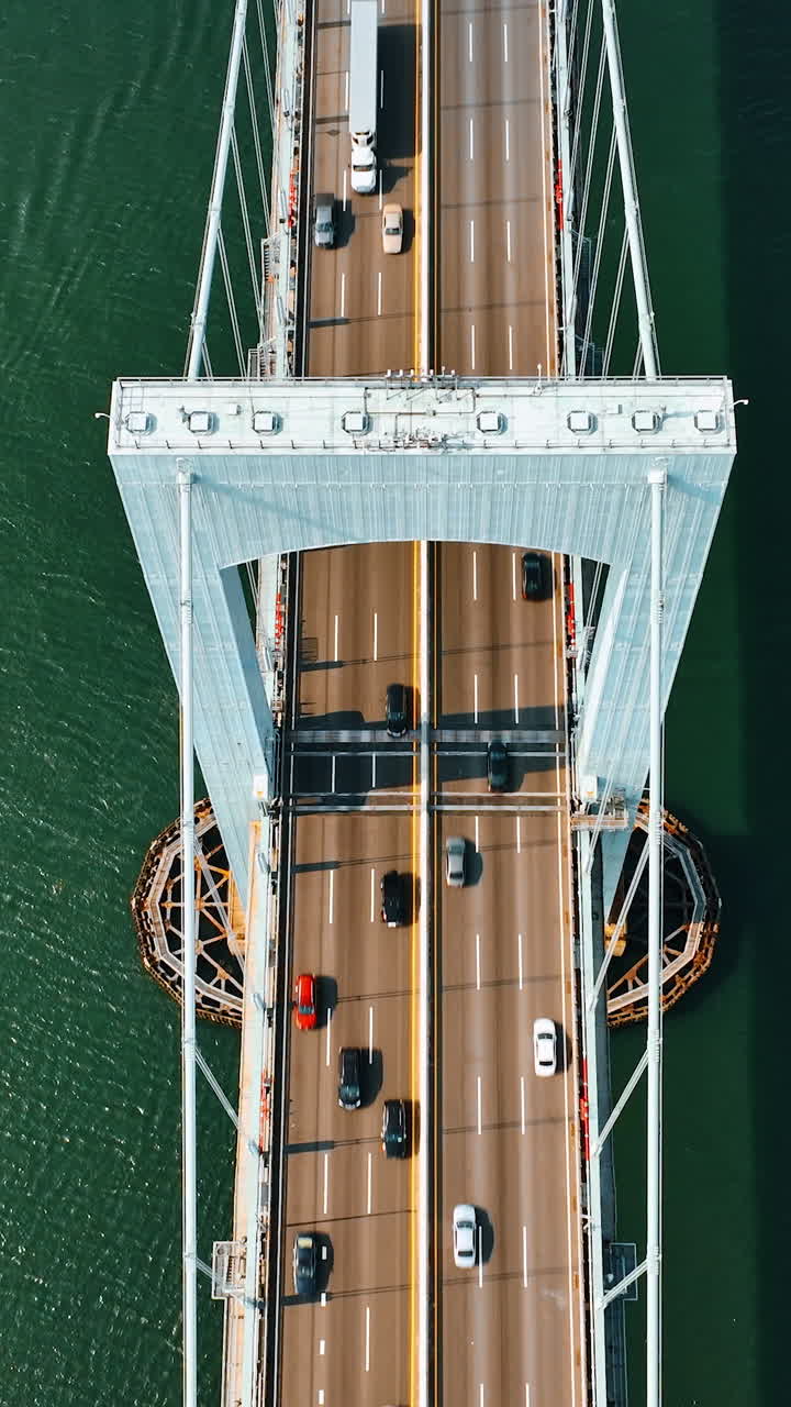Part of the suspension bridge over sea-green water. Cars move by the roads on the bridge under the support. Motor boat is on the water. Top view. Vertical video