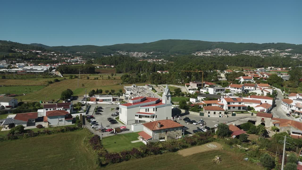 Vista aérea de drone da Igreja Paroquial de Lijó em Barcelos, Portugal, mostrando cemitério da igreja paroquial, casas da aldeia, campos agrícolas e colinas verdes na região do Minho