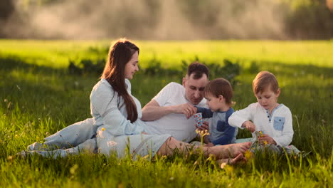 Vater,-Mutter-Und-Zwei-Kinder-Sitzen-Bei-Sonnenuntergang-Auf-Einer-Wiese-Und-Essen-Im-Sommer-Ein-Eis-Bei-Einem-Picknick.