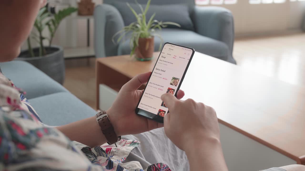 Man Sitting On Couch Using Smartphone Buys Food In Internet Shop. Male Selects Food In Food Online Delivery Apps