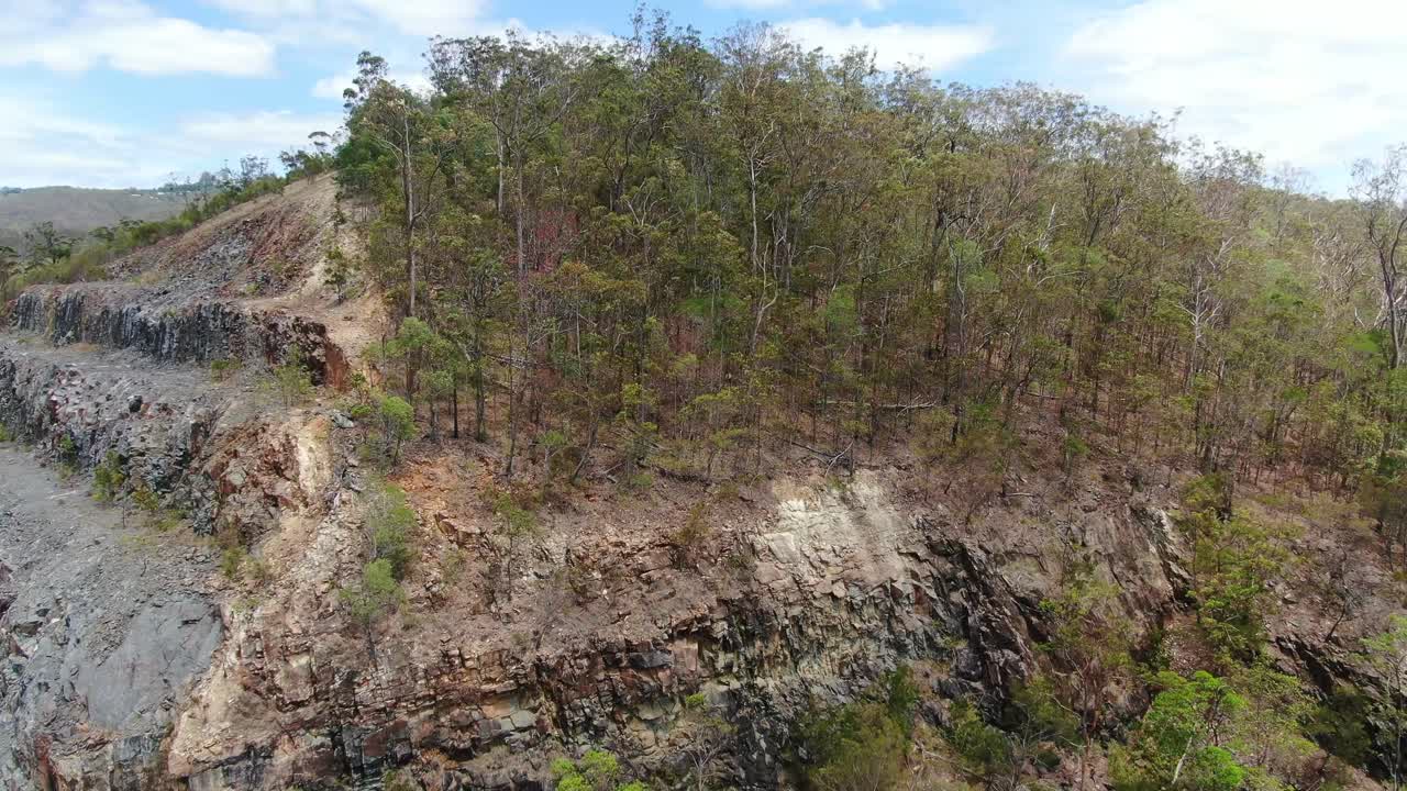 Drone Ascending at quarry rock wall rising up to reveal bush-land and  hinterland