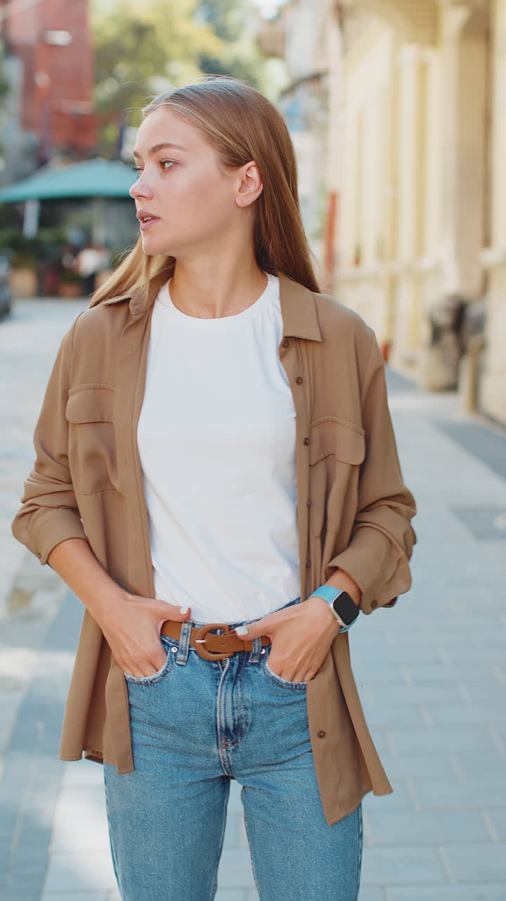 Serious dissatisfied young caucasian woman standing and looking for someone waiting on city street